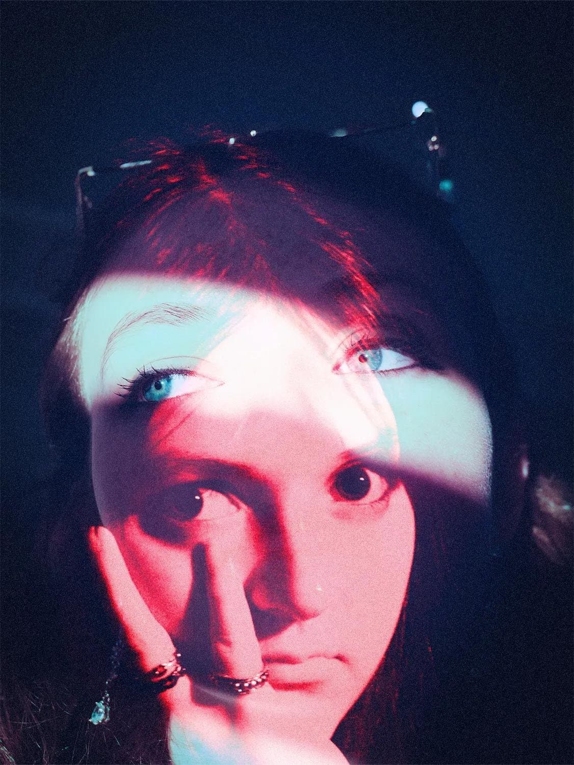 Close-up portrait of a woman washed in red and blue light, her ringed hand resting near her face — human-made reference photo on Slow Sync