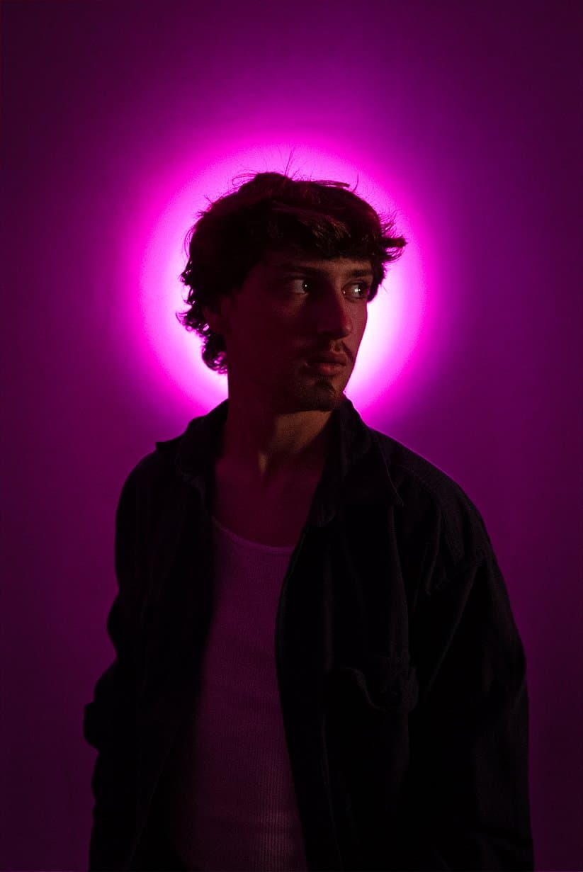 Young man in near-silhouette against a glowing violet and magenta halo of light — human-made reference photo on Slow Sync
